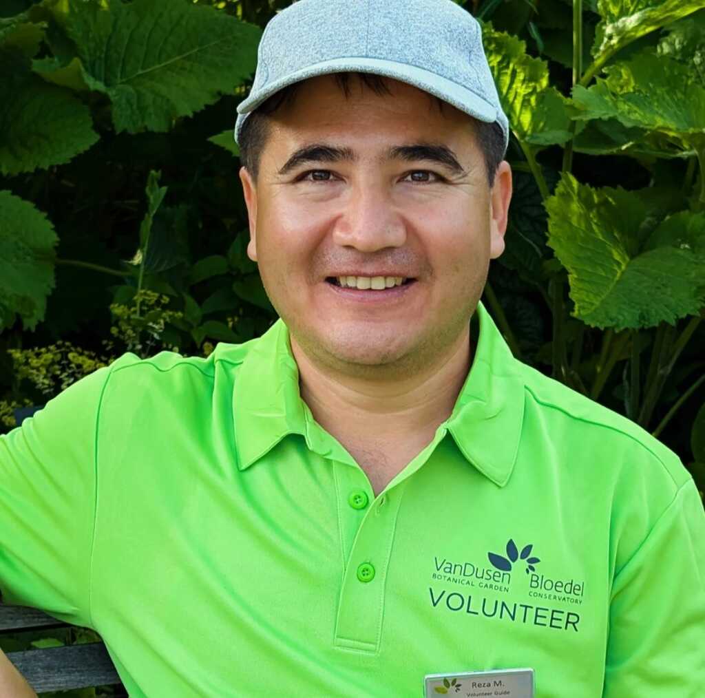 Reza smiling in front of lush greenery.
